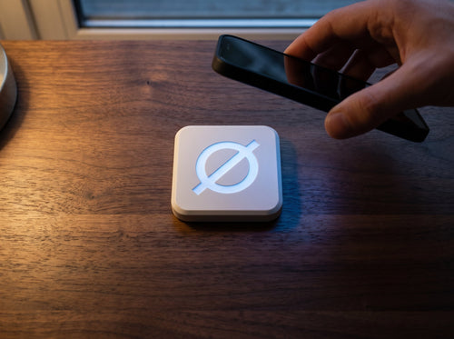 A phone lowering onto a white Null Tag on a walnut desk, blue NFC bloom